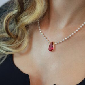 Close-up of a woman's neck adorned with a pearl and red gem necklace, showcasing elegance and luxury.
