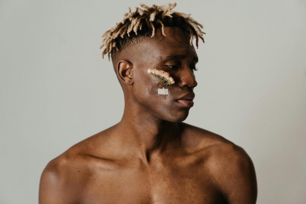 Conceptual portrait of a shirtless man with flowers on face, symbolizing natural beauty.
